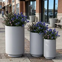 A striking trio of commercial-grade GFRC planters featuring a refined polished concrete finish, beautifully contrasted with lush architectural foliage to create an elegant focal point in a modern landscape design.